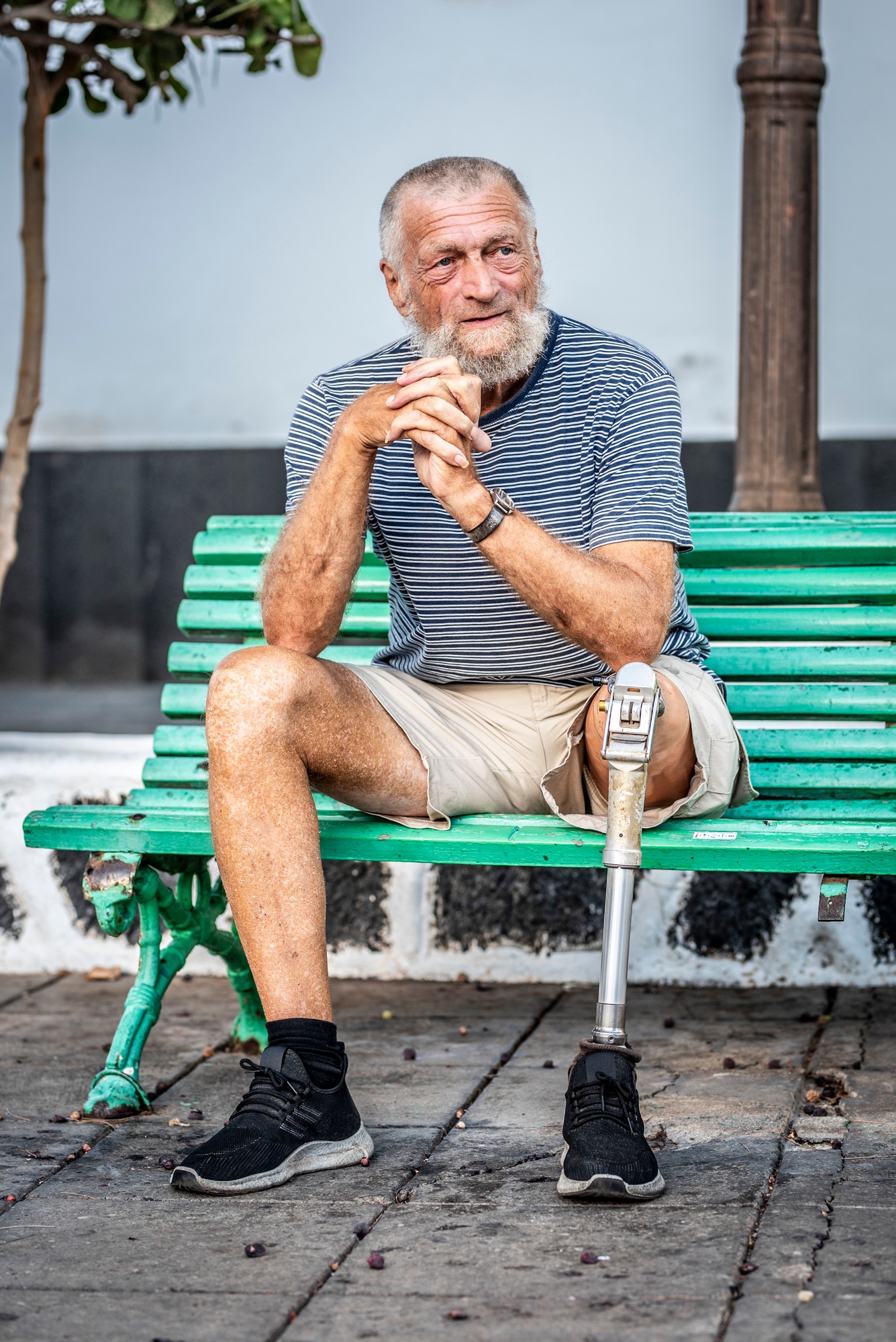 Elderly man with prosthetic leg left rests sitting on a park bench